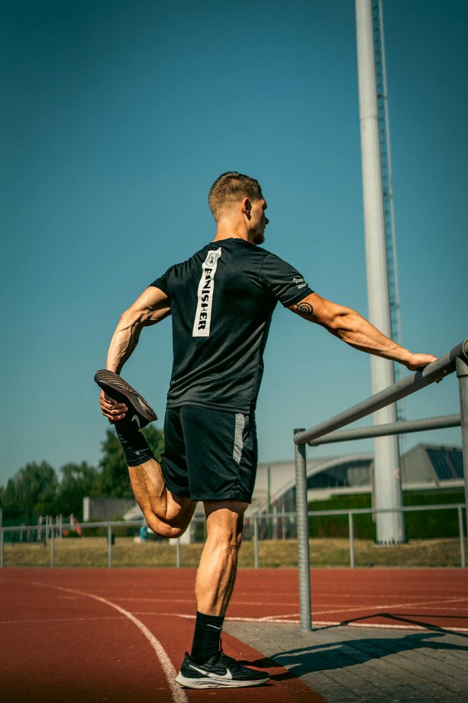 Young athletic man stretching on an outdoor track under clear blue skies.
