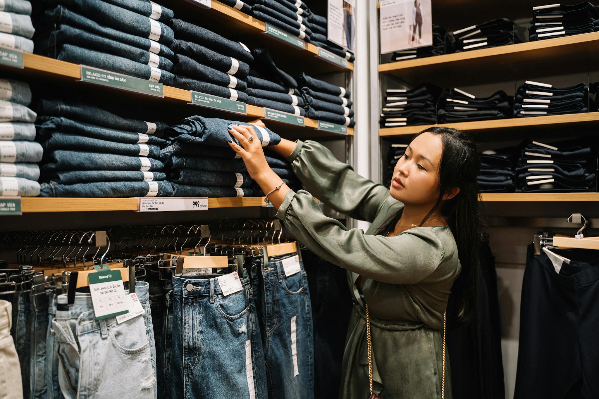 Asian woman browsing denim jeans on shelves in a clothing store.