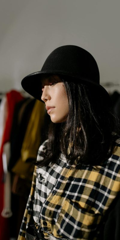 Stylish Asian woman wearing a black hat in a clothing shop, showcasing modern fashion.
