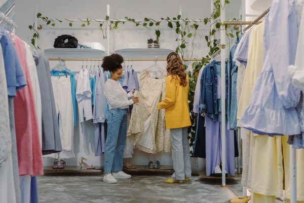 Two women shopping for trendy outfits in a modern clothing boutique filled with colorful garments.