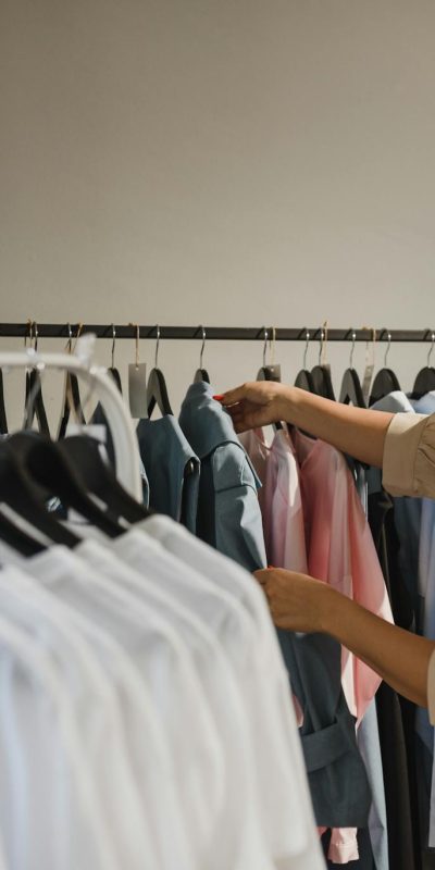 Woman browsing clothes in a boutique, selecting from a variety of stylish shirts on a rack.