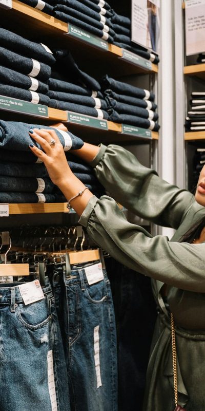 Asian woman browsing denim jeans on shelves in a clothing store.