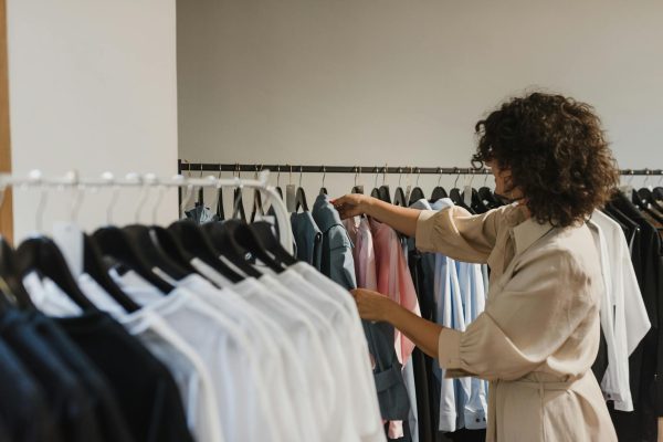 Woman browsing clothes in a boutique, selecting from a variety of stylish shirts on a rack.